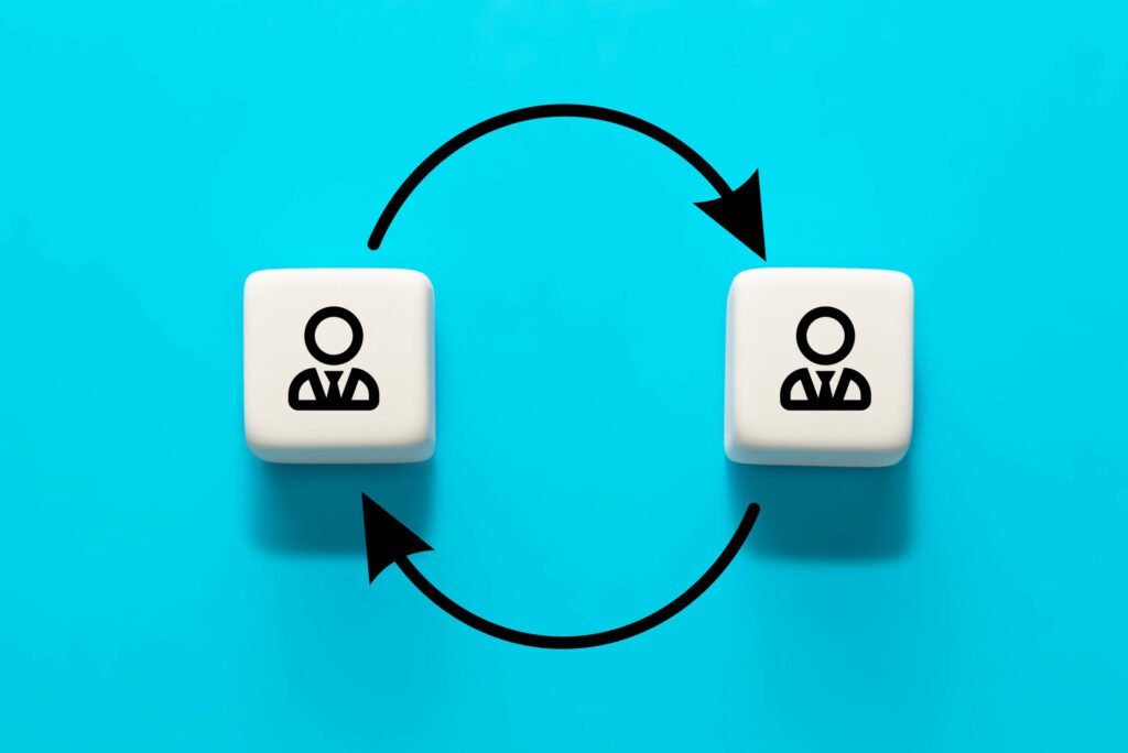 A imagem mostra dois cubos brancos com uma pessoa em cada um deles. Os cubos estão conectados por uma seta que vai de um cubo para o outro. A imagem representa a mudança de emprego. A seta que conecta os dois cubos pode sugerir que a pessoa está mudando de um emprego para outro.