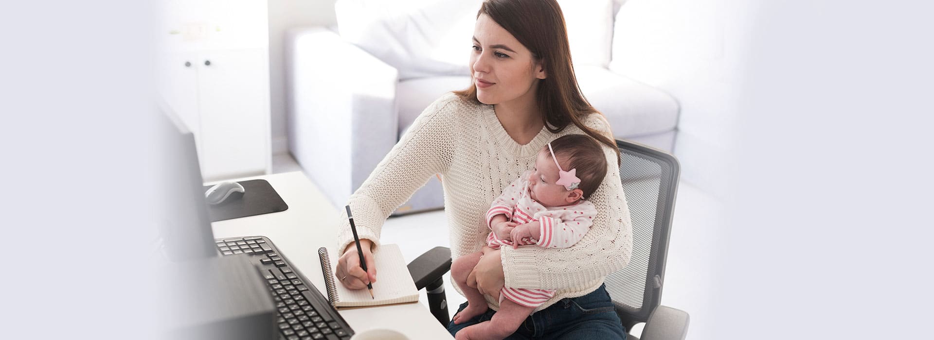 Mulher com um bebê no colo e fazendo anotações